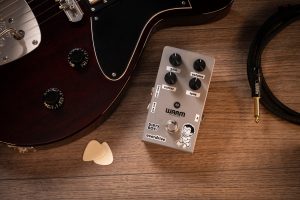 Warm Audio Dirty Boy Jr. Overdrive pedal next to a guitar on a table.